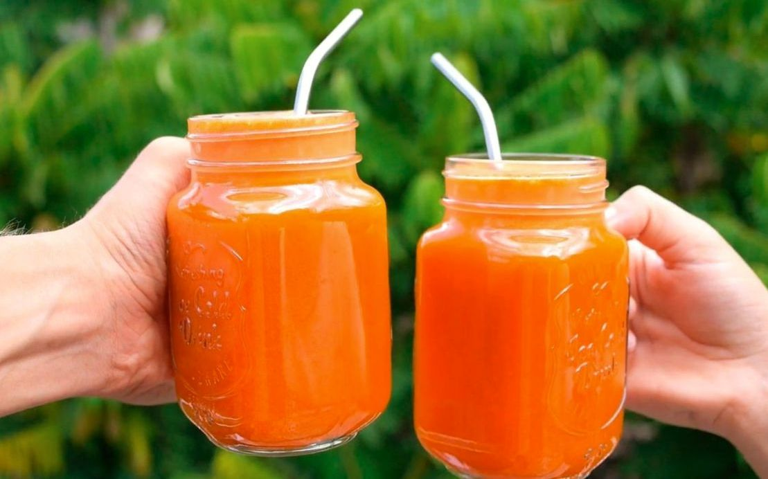 A tropical smoothie in a tall glass with fresh fruit on top